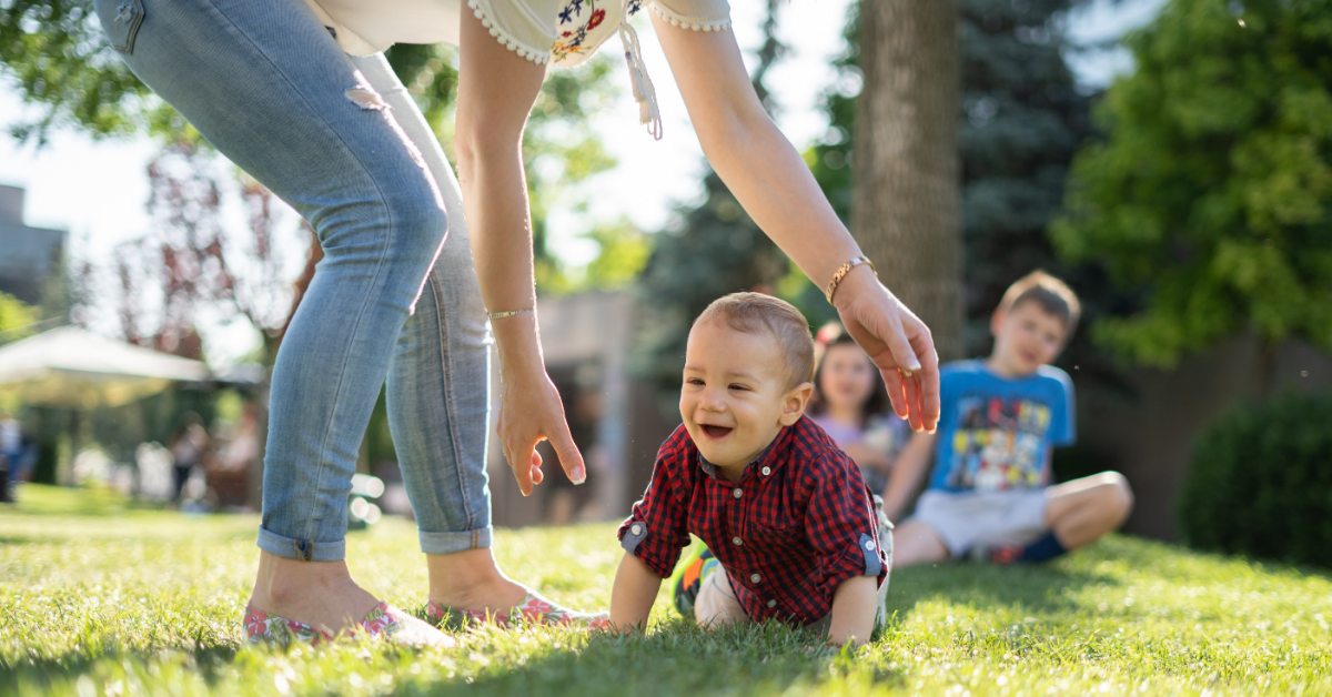 Young child crawling across a green lawn at a family gathering.